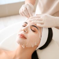 Cosmetologist applying sheet mask on woman's face in beauty salo